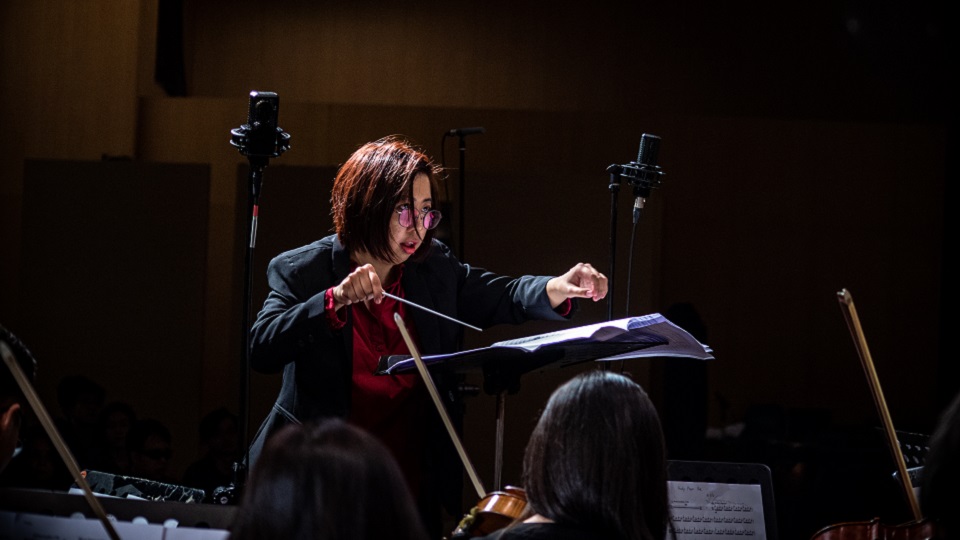 Photo of female alumna in concert dress, conducting an ensemble.